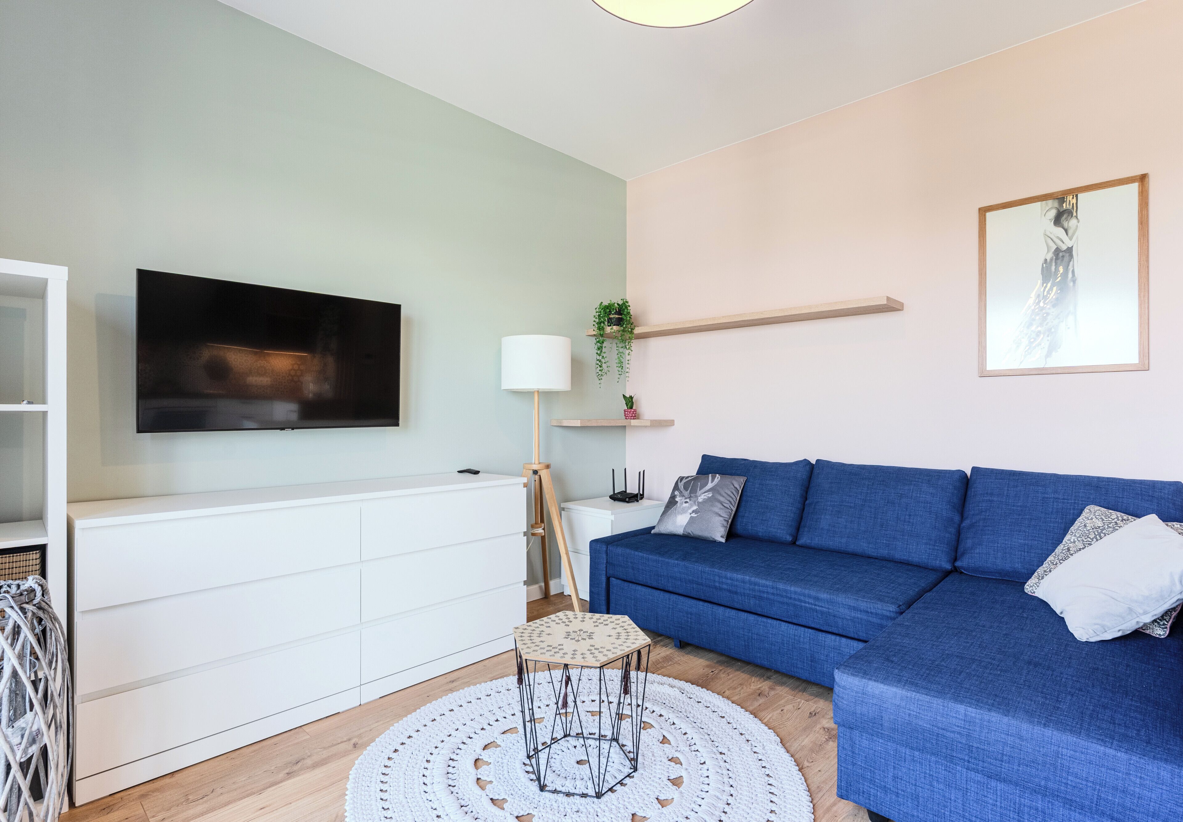 Una sala de estar moderna con un sofá azul, un mueble blanco, un televisor y un tapete redondo blanco.