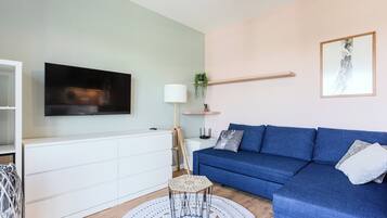 Una sala de estar moderna con un sofá azul, un mueble blanco, un televisor y un tapete redondo blanco.