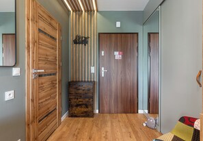 A hallway with wooden flooring, a wooden door with a handle, a small cabinet, and a cat-shaped cushion on the floor.