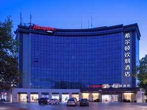 A modern hotel with a curved facade, multiple entry points, and a prominent brand sign. - Hampton by Hilton Yiwu international  (Jinhua)
