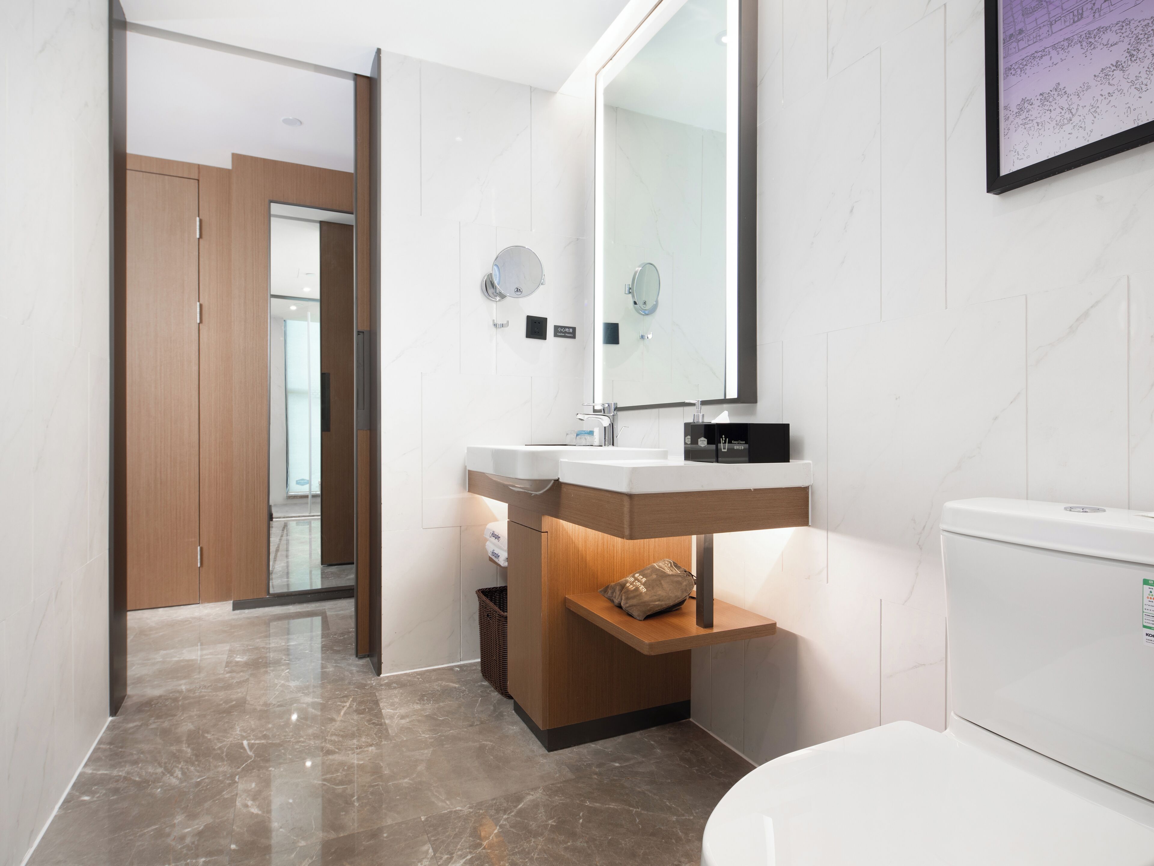 A modern bathroom with a marble floor, a wooden vanity, a white toilet, and a large mirror.