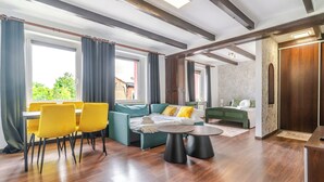 Habitación de hotel moderna con zona de comedor, sofá, cama y vista a zonas verdes.