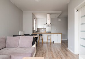 Eine moderne Küche mit einer zentralen Kochinsel, ein Essbereich mit einer Couch und Stühlen sowie ein Flur zu einer Tür.