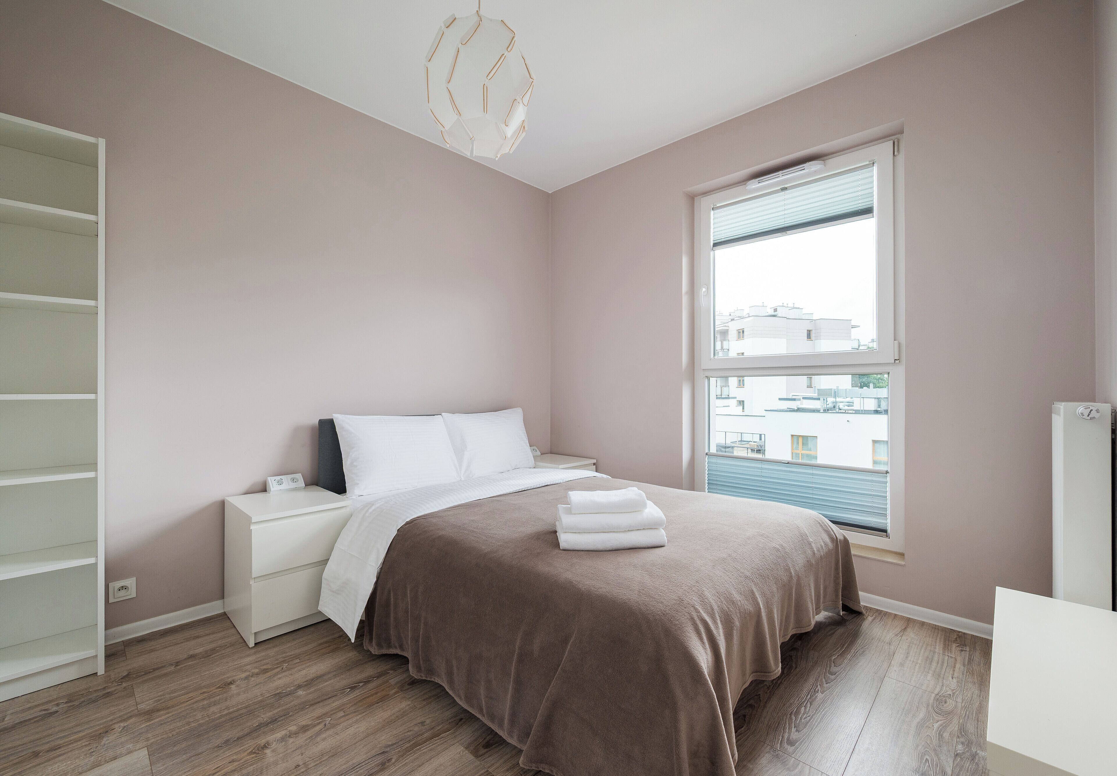 A bedroom with a bed, bedside tables, a wardrobe, a window with blinds, and a radiator.
