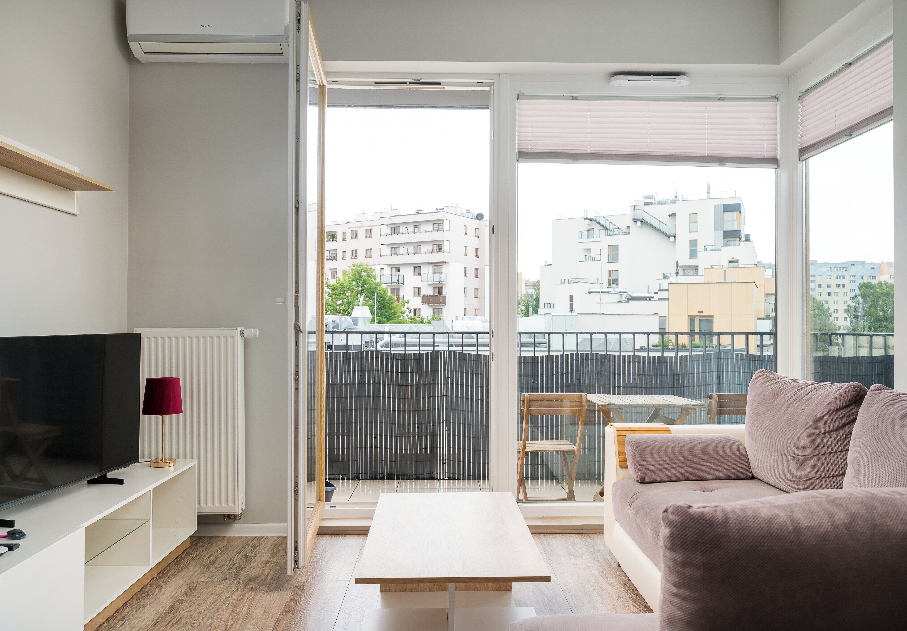 A modern living room with a flat-screen TV, a red lamp, a white radiator, a wooden coffee table, and a sofa.