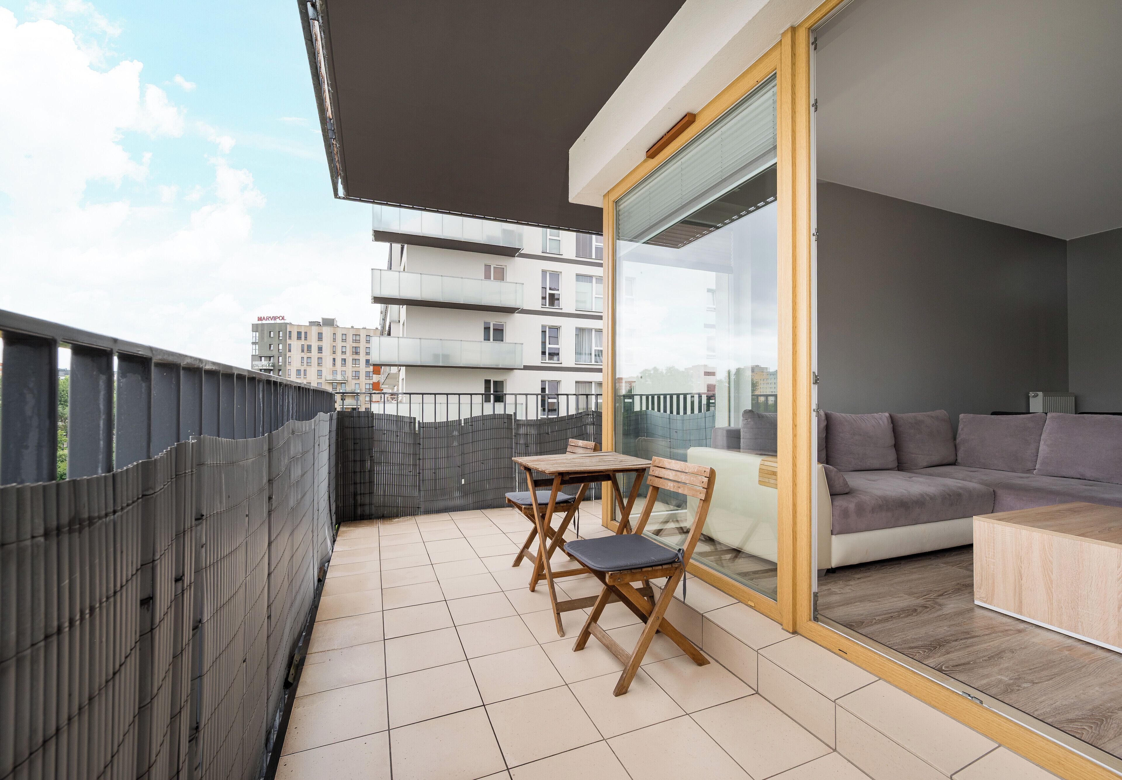 A balcony with a table and chairs, a sofa, and a sliding glass door leading to an interior space.