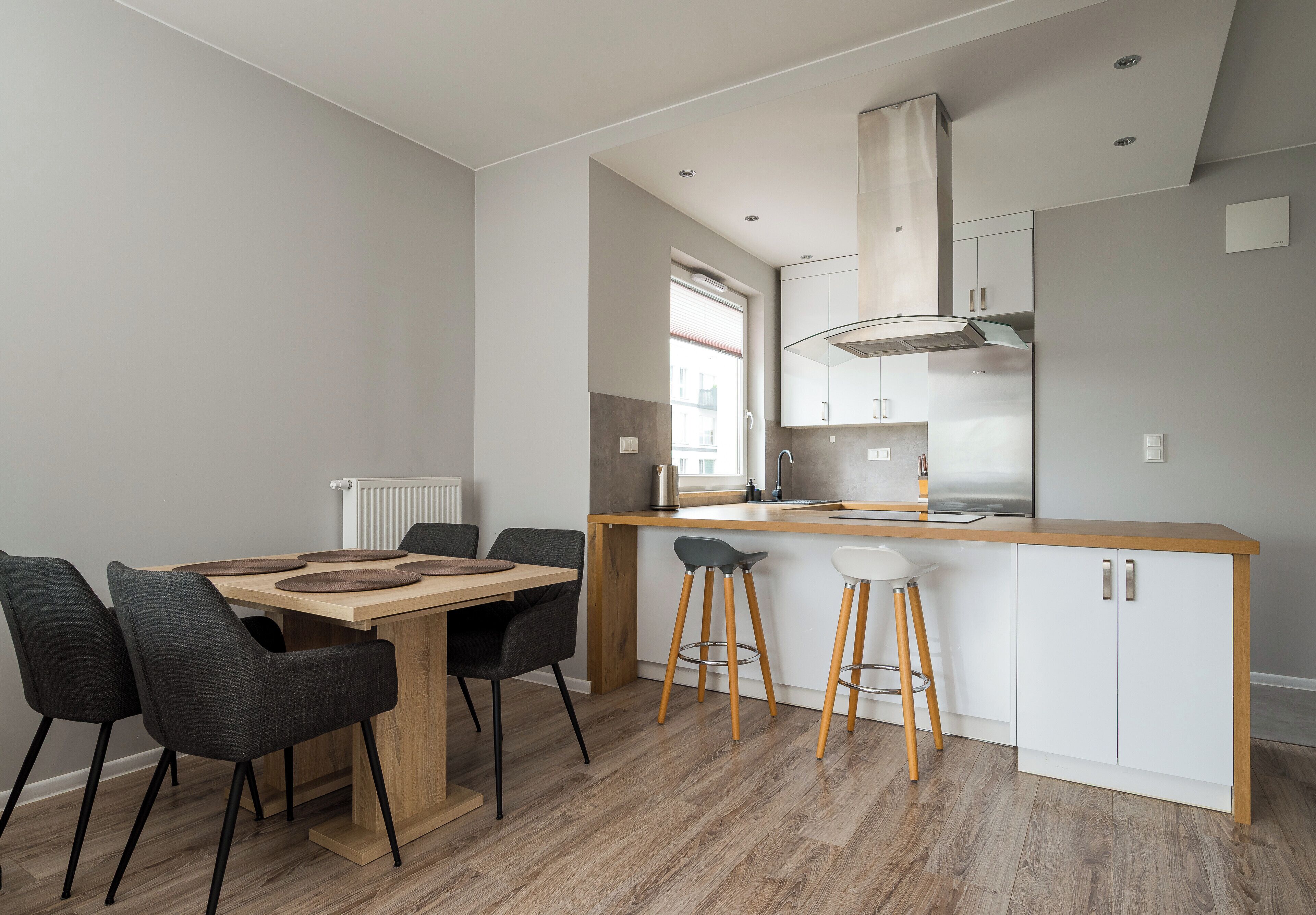 A modern kitchen with a central island, bar stools, and a dining table with chairs.