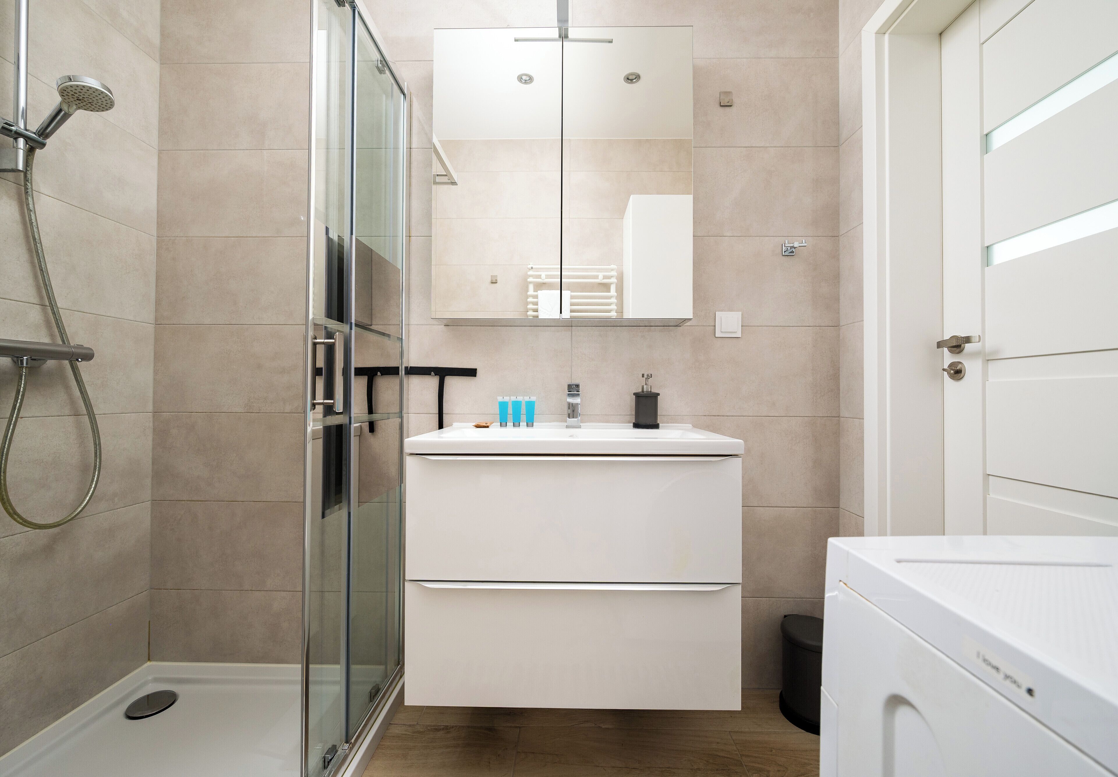 Une salle de bain moderne avec une douche à parois de verre, un lavabo blanc avec un miroir au-dessus et des toilettes blanches.