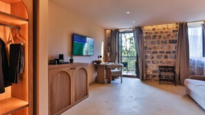 Ein Hotelzimmer mit Holzschrank, Fernseher, kleinem Tisch mit Stuhl, Balkon mit Steinwand und einer Couch.