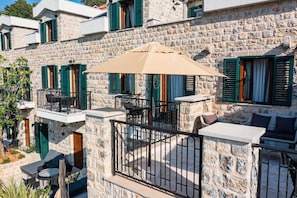 A stone building with balconies, outdoor seating, and a large umbrella. - Boutique Hotel Ruzmarin SPA & Garden (Budva)