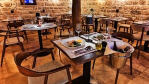 Ein Restaurant mit Steinwänden, mehreren Tischen, Stühlen und einem an der Wand befestigten Fernseher.