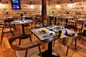A restaurant with stone walls, multiple tables, chairs, and a television mounted on the wall. - Boutique Hotel Ruzmarin SPA & Garden (Budva)