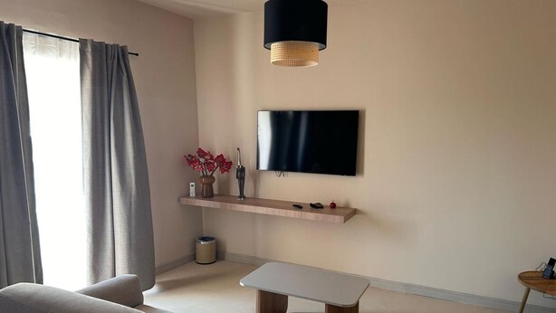 Ein modernes Wohnzimmer mit einer Couch, einem Couchtisch, einem an der Wand befestigten Fernseher und einer Pendelleuchte.