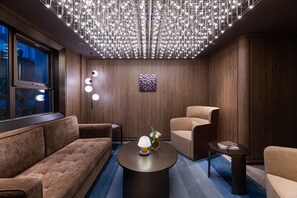 A modern lounge with a sofa, armchair, and round coffee table, featuring a unique ceiling light fixture and a decorative wall piece. - Crystal Hotel Beijing Chongwenmen (Beijing)