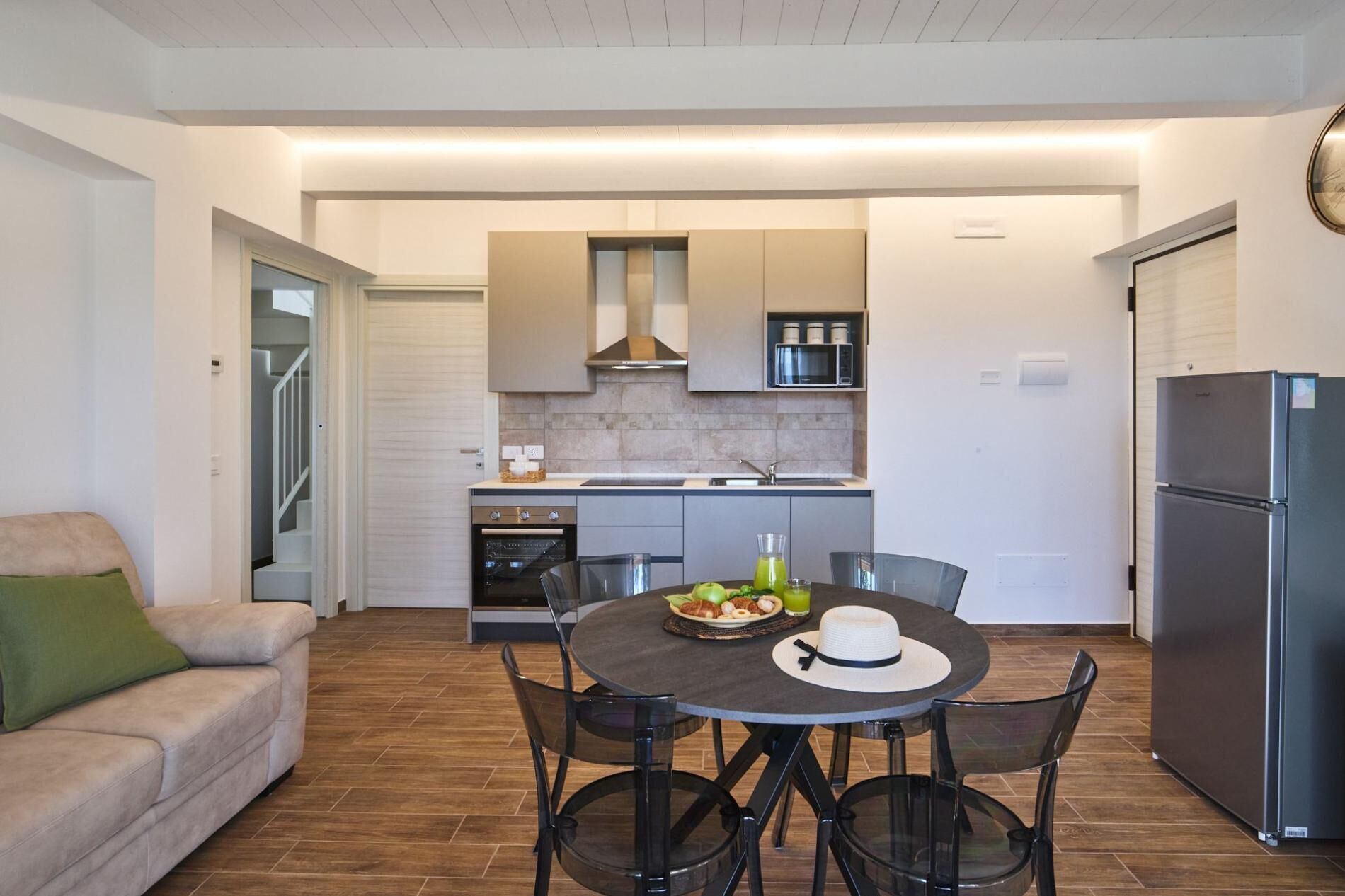A modern kitchen with a dining area, a sofa, and a refrigerator.