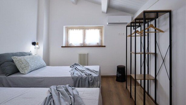 A bedroom with two beds, a window, an air conditioning unit, and a wooden wardrobe with hanging space. - Villa Esther, 7 bedrooms, pool, A/C, EV charger, pet friendly, Marche (Fermignano)
