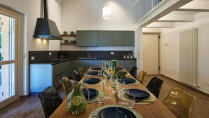 A modern dining area with a long table set for a meal, a kitchen in the background, and a staircase leading to an upper level. - Villa Esther, 7 bedrooms, pool, A/C, EV charger, pet friendly, Marche (Fermignano)