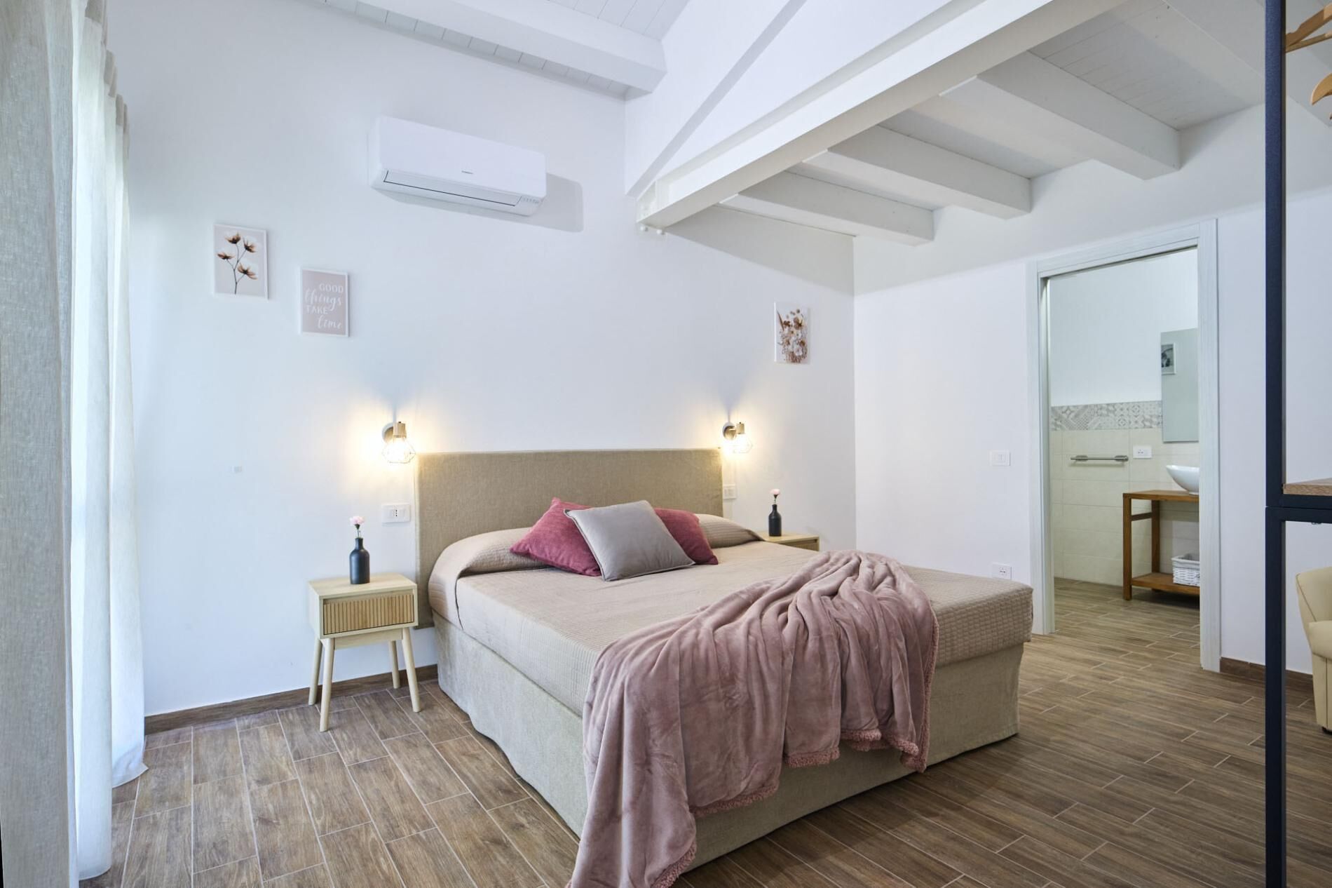 Een slaapkamer met een bed, nachtkastjes, een airconditioning en een zichtbare badkamer door een open deur.