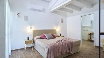 Een slaapkamer met een bed, nachtkastjes, een airconditioning en een zichtbare badkamer door een open deur.