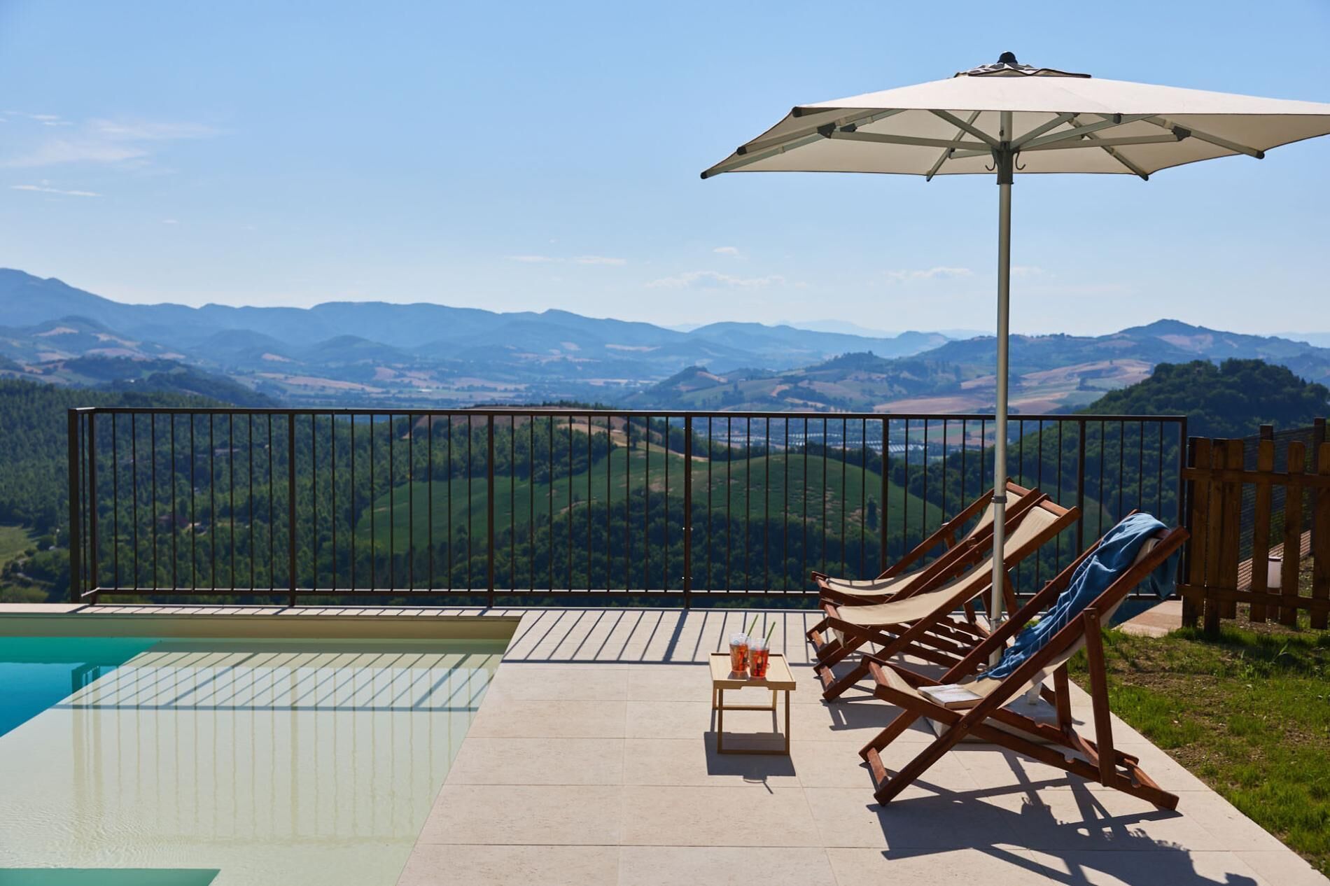 Un espace aménagé au bord de la piscine, avec des chaises longues et une table, offrant une vue sur un paysage montagneux.