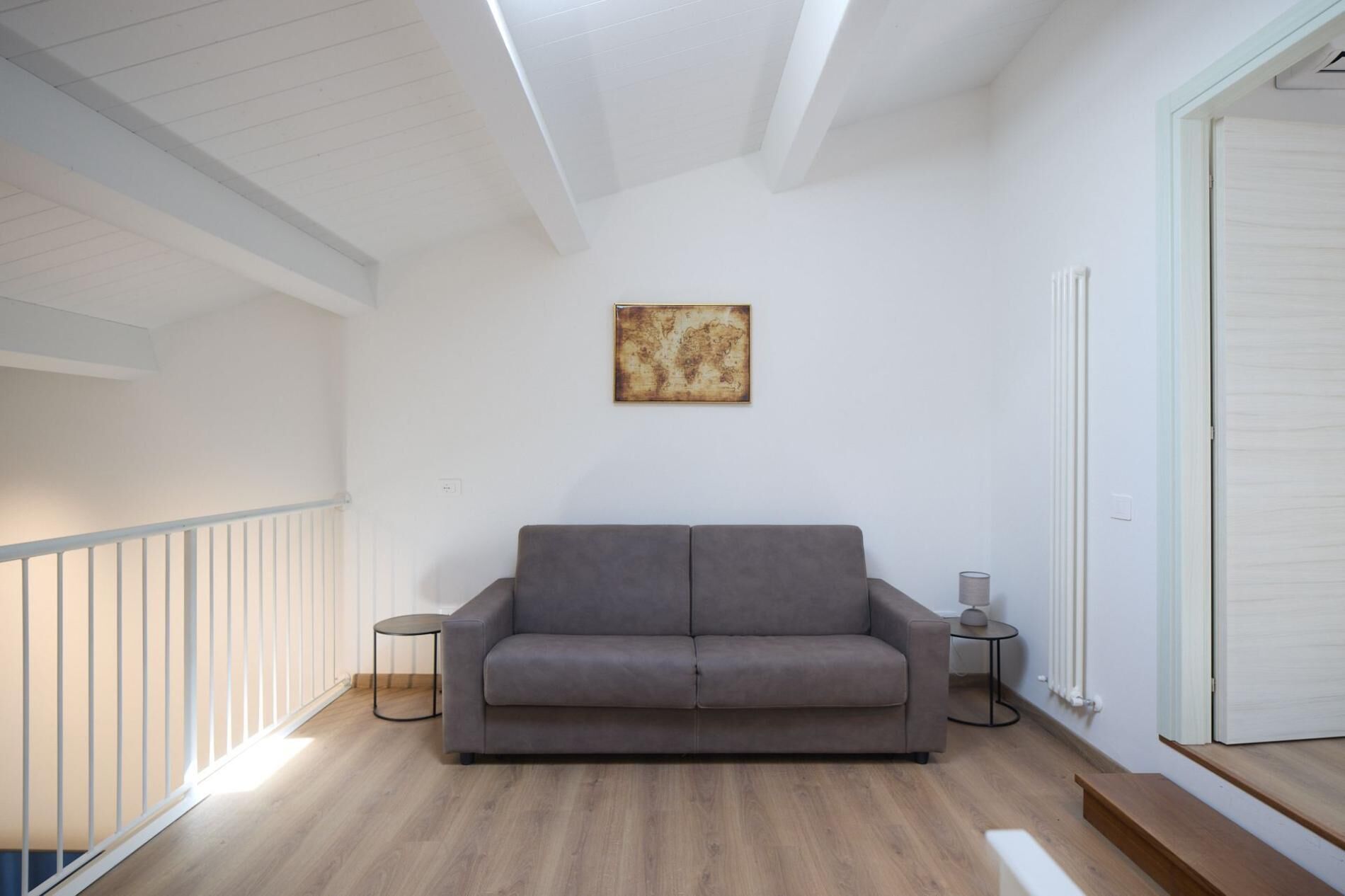 Un salon moderne avec un canapé gris, une petite table ronde surmontée d’une lampe et une œuvre d’art représentant une carte du monde accrochée au mur.