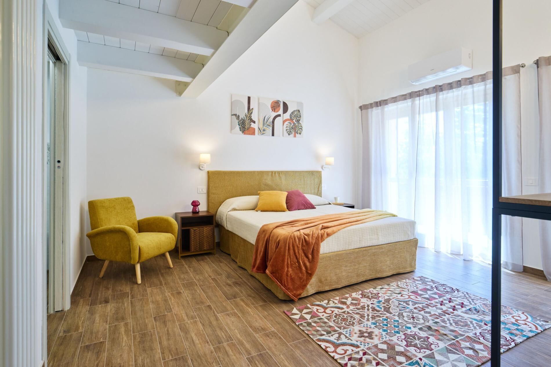 A hotel room with a bed, a chair, a nightstand, and a patterned rug.