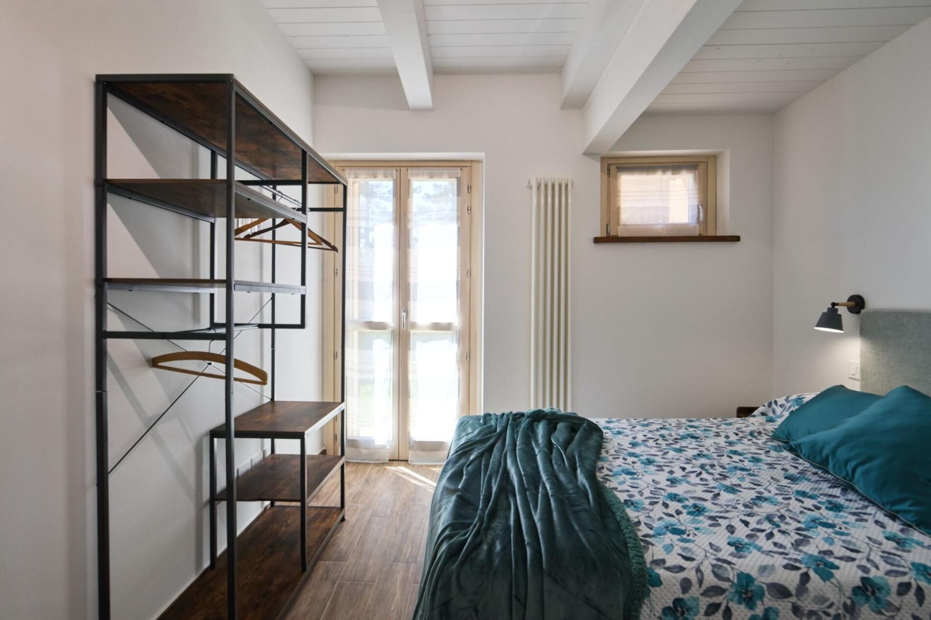 Ein Schlafzimmer mit Bett, einem Kleiderschrank mit Ablagen, einem Heizkörper und einem Fenster.