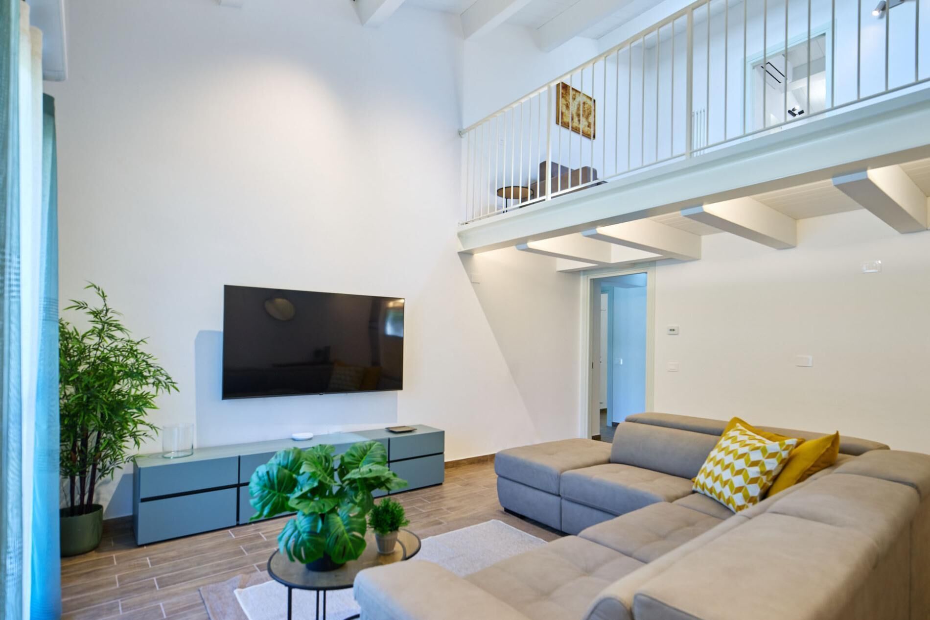 Een moderne woonkamer met een flatscreen televisie, een grijze zithoek en een balkon met een hekwerk.