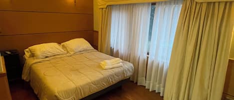 Une chambre d’hôtel avec un lit, un plancher en bois, une table de chevet et une fenêtre avec des rideaux.