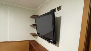A room with a mounted television on the wall, wooden benches, and a radiator. - Hotel Peregrino Suites (Concepción)