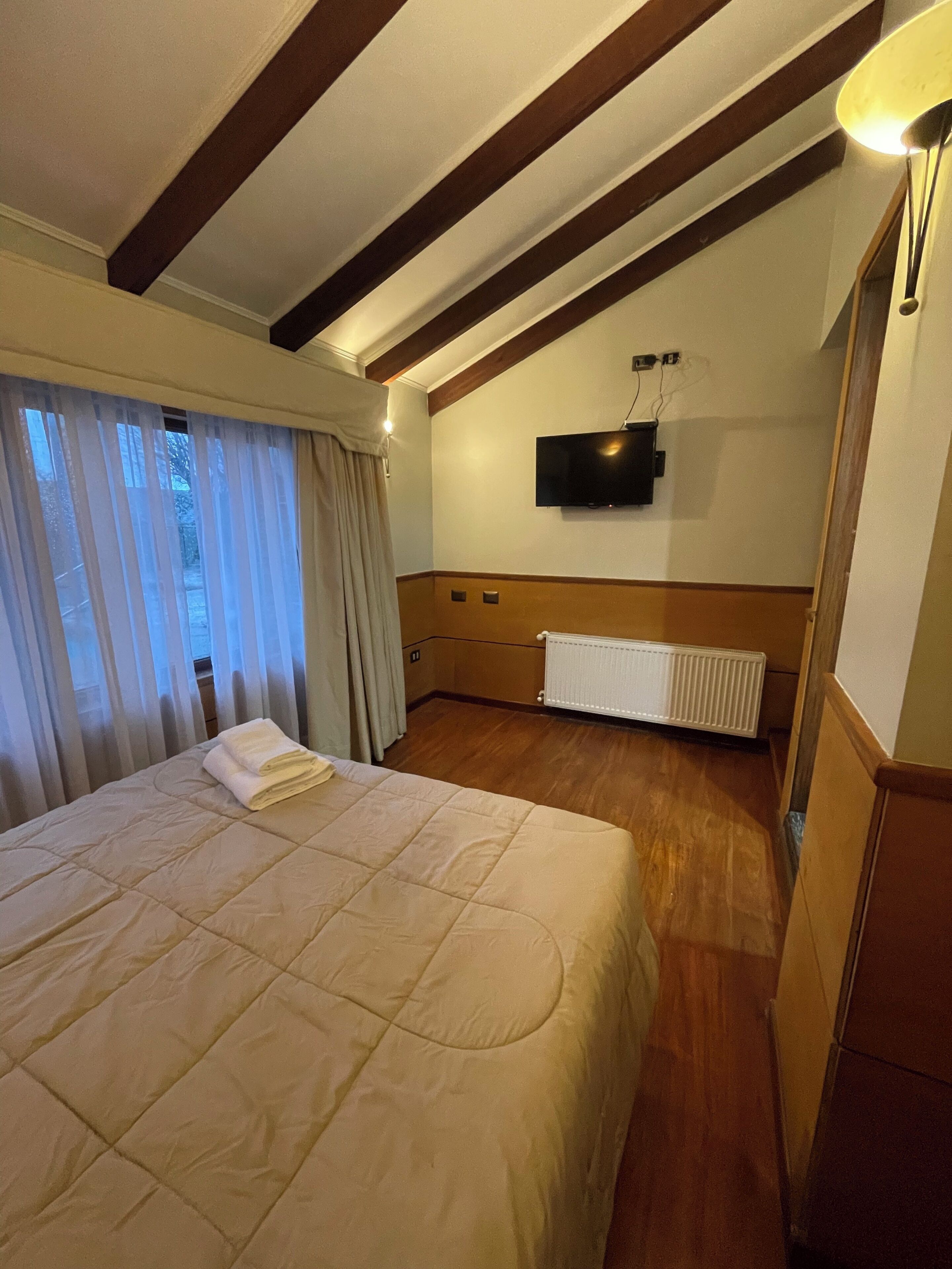 Ein Hotelzimmer mit einem großen Bett, Holzbalken an der Decke, einem Wand-Fernseher und einer Heizung.