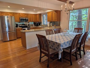 Une cuisine moderne avec des meubles en bois, des appareils électroménagers en acier inoxydable et un coin repas comprenant une table et des chaises.