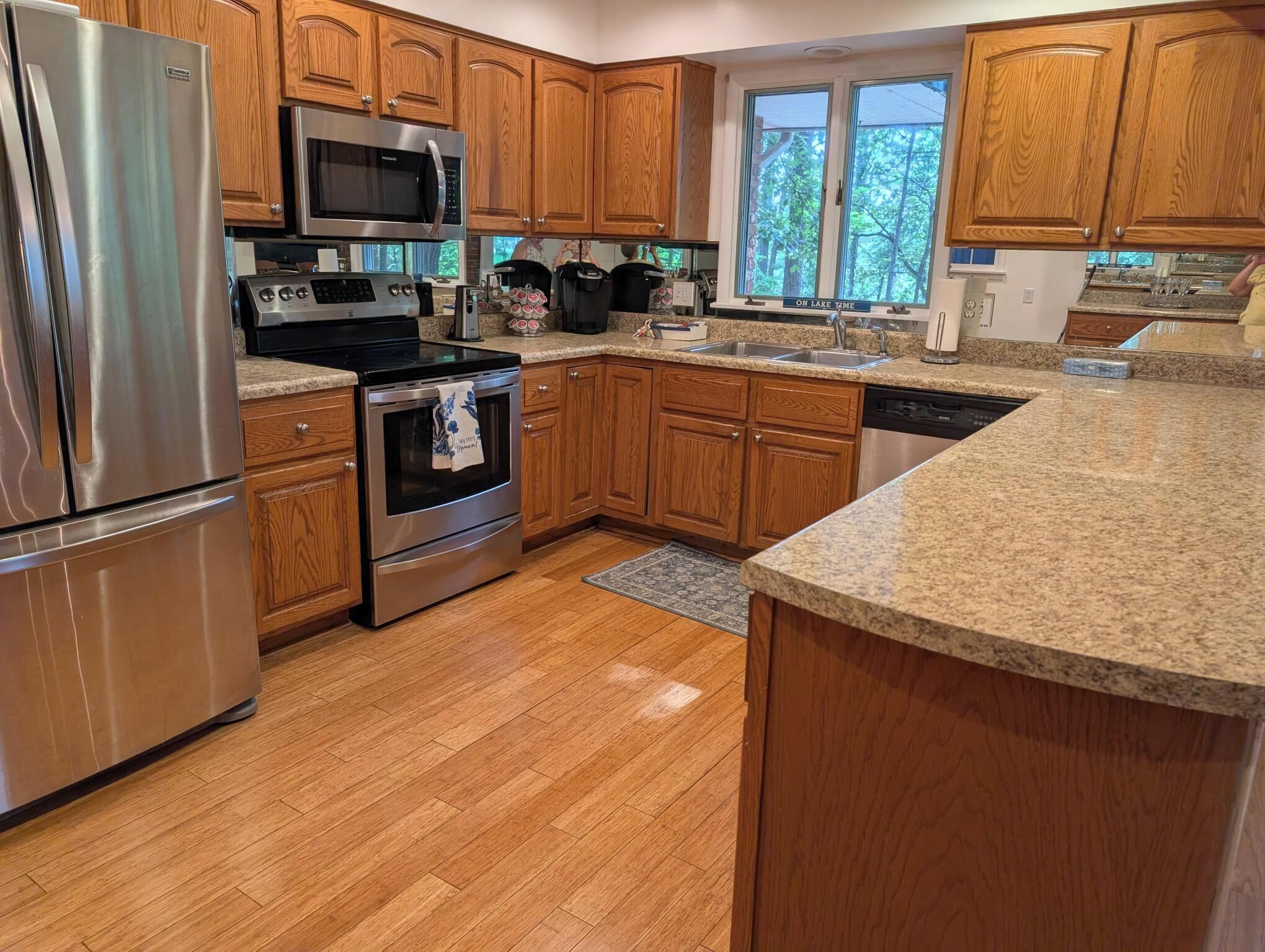 A kitchen with wooden cabinets, stainless steel appliances, granite countertops, and a window with a view of trees.
