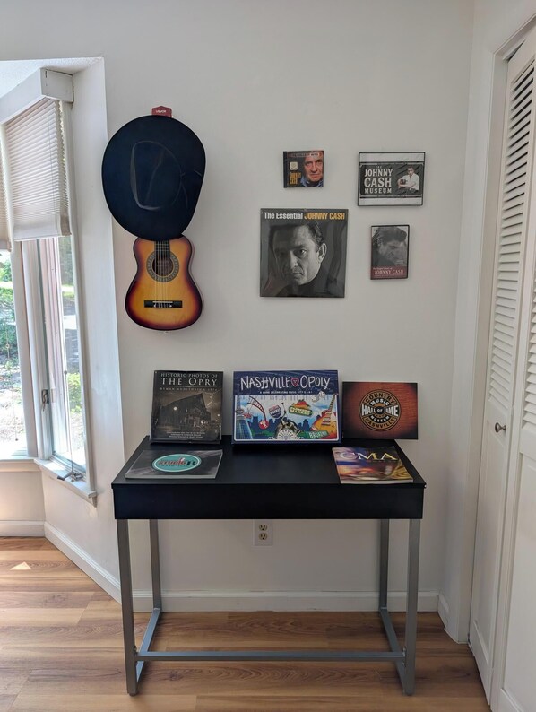 A wall with framed memorabilia and a guitar, a table with books and a CD, and a window with blinds.