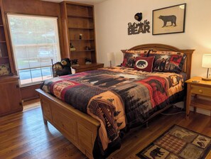 A cozy bedroom with a wooden bed, a bear-themed headboard, and a window with a view of the outdoors. - Beautiful & Spacious 3 bedroom/3 bath home with stunning views of Norfolk Lake (mountain home)