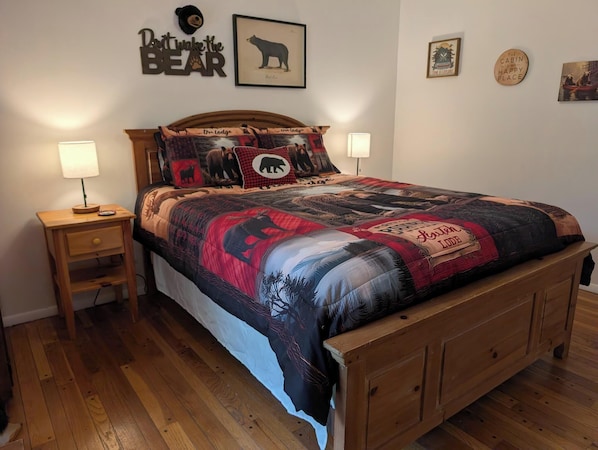 Un lit avec une couette à motifs d’ours, une tête de lit en bois, deux lampes de chevet et une petite table de chevet en bois avec une lampe.