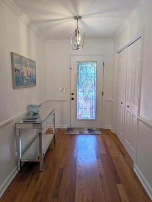 A hallway with a wooden floor, a glass door with a stained glass window, a painting on the wall, and a metal console table. - Beautiful & Spacious 3 bedroom/3 bath home with stunning views of Norfolk Lake (mountain home)