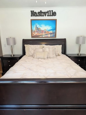 A hotel room with a bed, two nightstands, a lamp on each nightstand, a framed picture of a cityscape on the wall, and a sign above the bed that reads 'Nashville'. - Beautiful & Spacious 3 bedroom/3 bath home with stunning views of Norfolk Lake (mountain home)
