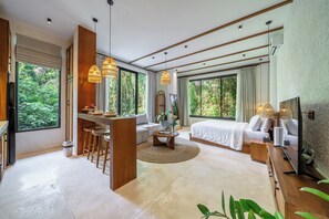 Una habitación de hotel moderna con una cama grande, un área de estar con una mesita de centro y una kitchenette.