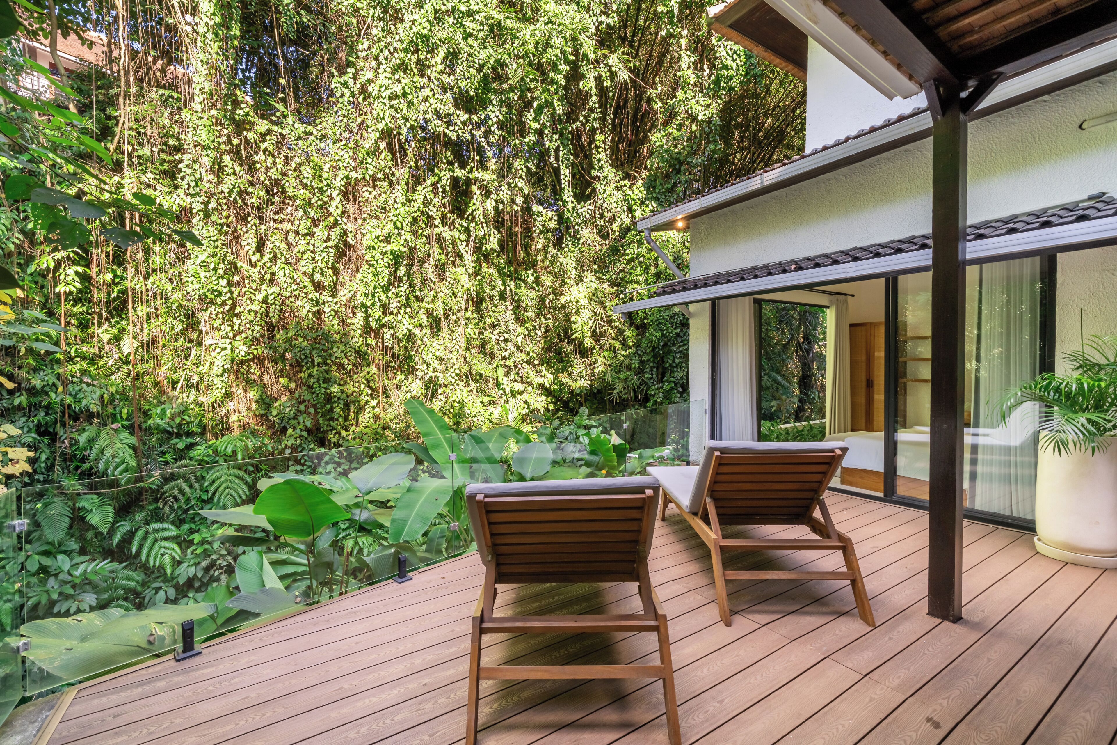 A wooden deck with two chairs, overlooking a lush garden with dense foliage and a modern building with large windows.