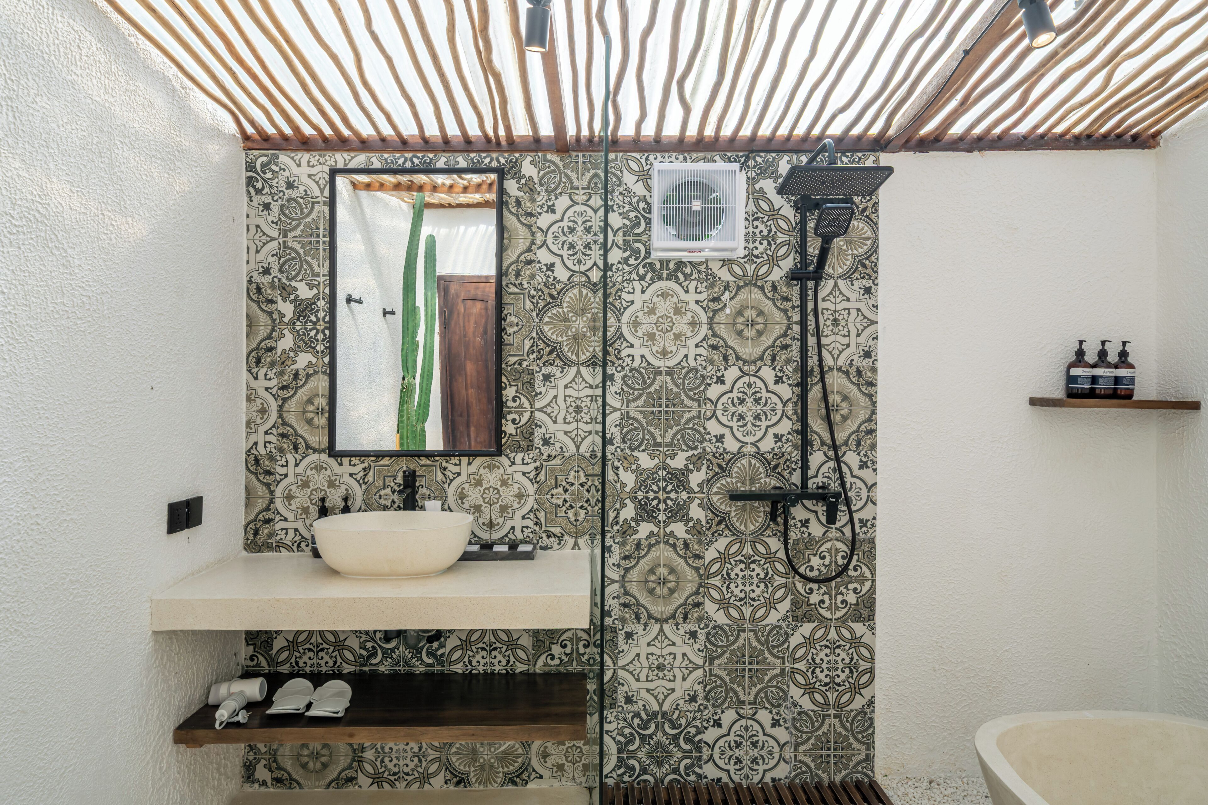 A bathroom with a white sink, a mirror, a shower, and patterned tiles.