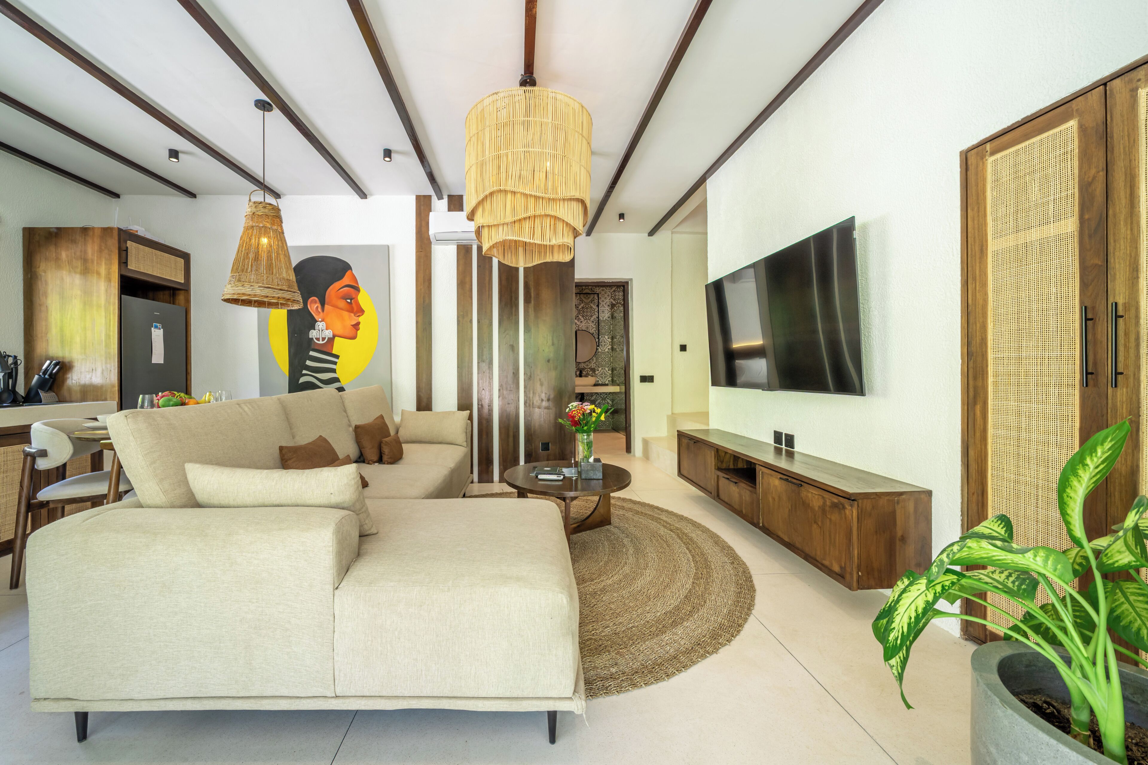 Una sala de estar moderna con un sofá modular, una mesa de centro redonda, un televisor montado en la pared y una planta grande en maceta.