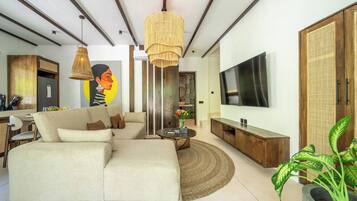 Una sala de estar moderna con un sofá modular, una mesa de centro redonda, un televisor montado en la pared y una planta grande en maceta.