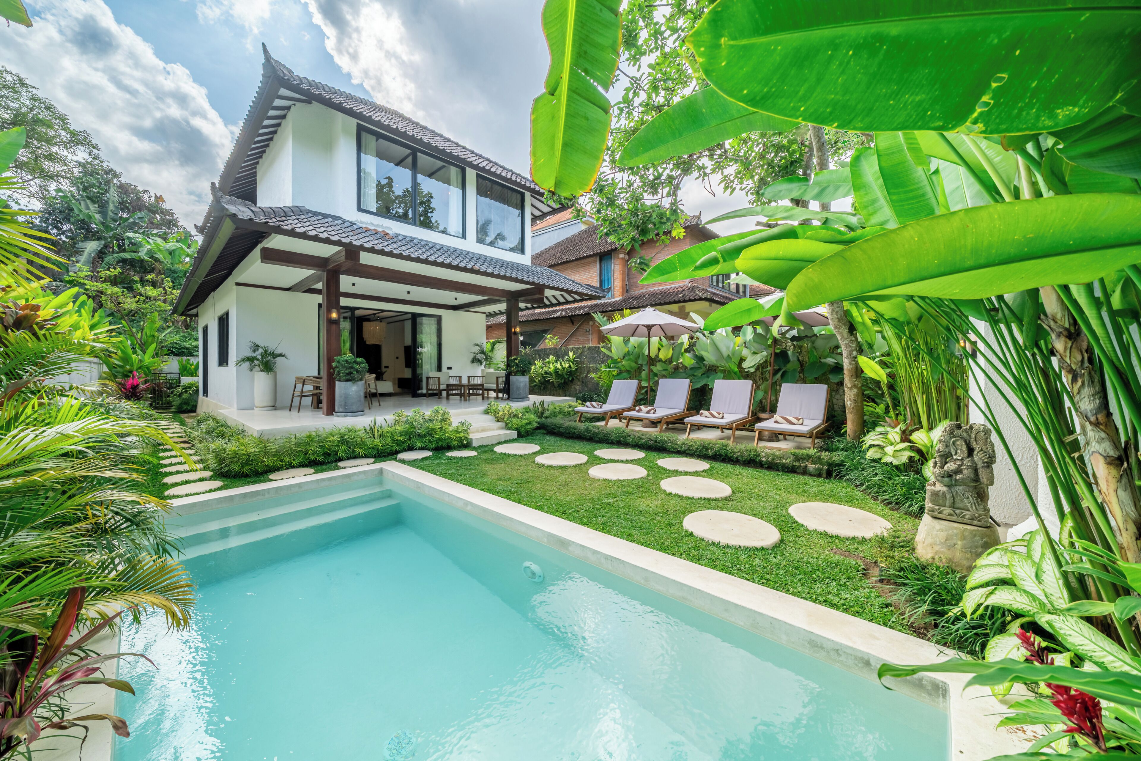 Una casa moderna con piscina, rodeada de exuberante vegetación y un techo tradicional de tejas.