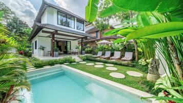 Una casa moderna con piscina, rodeada de exuberante vegetación y un techo tradicional de tejas.