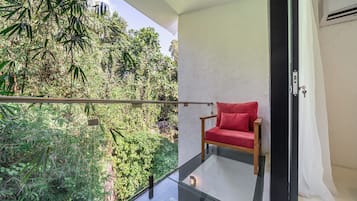 A balcony with a glass railing overlooking dense foliage, a red cushioned chair, and a white wall with a door.