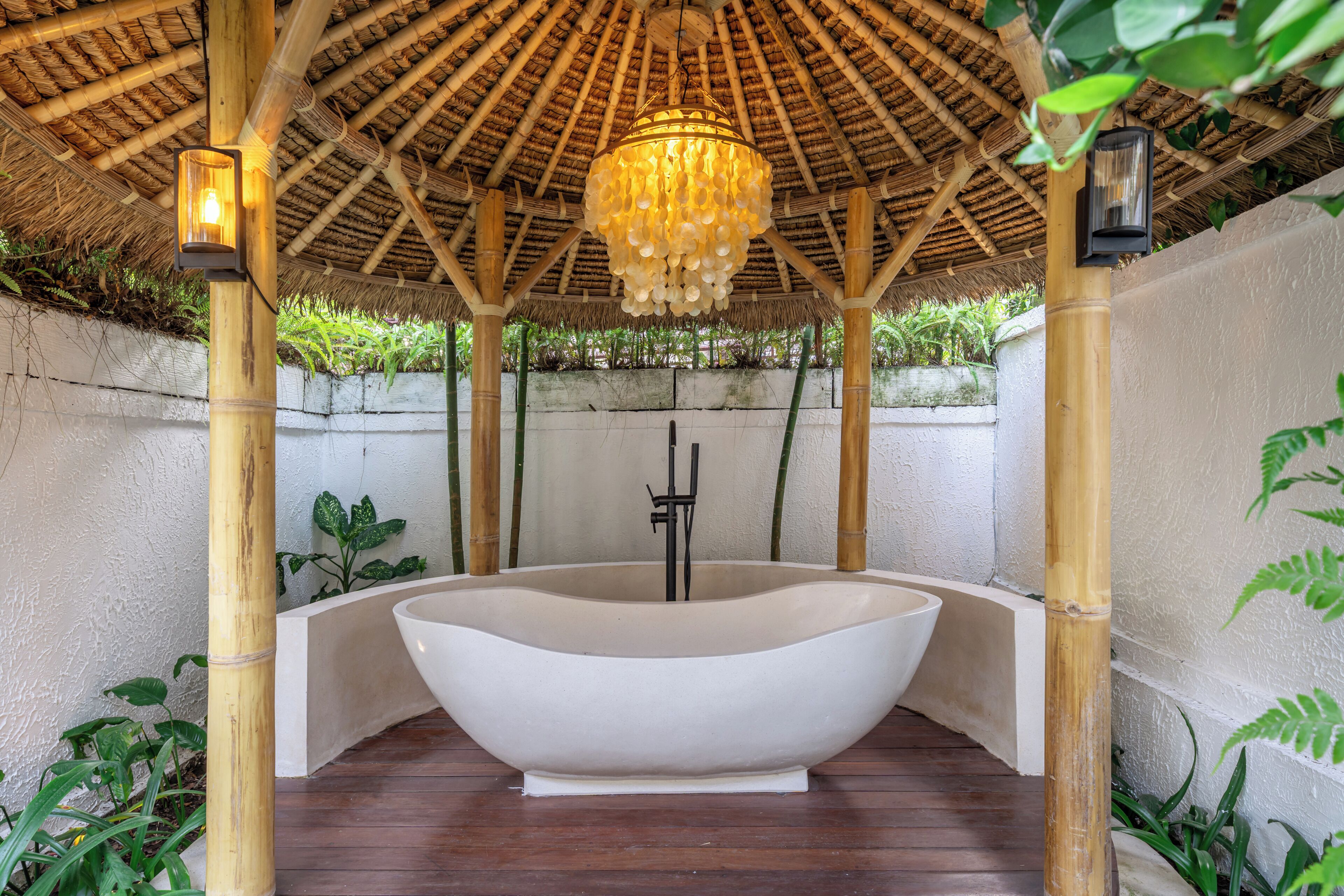 A large freestanding bathtub under a bamboo gazebo with a hanging light fixture.