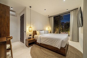 A modern bedroom with a large bed, bedside lamps, a wooden desk, and a view of the outdoors through a large window. - Sacred Jungle Villas & Apartments (Gianyar)