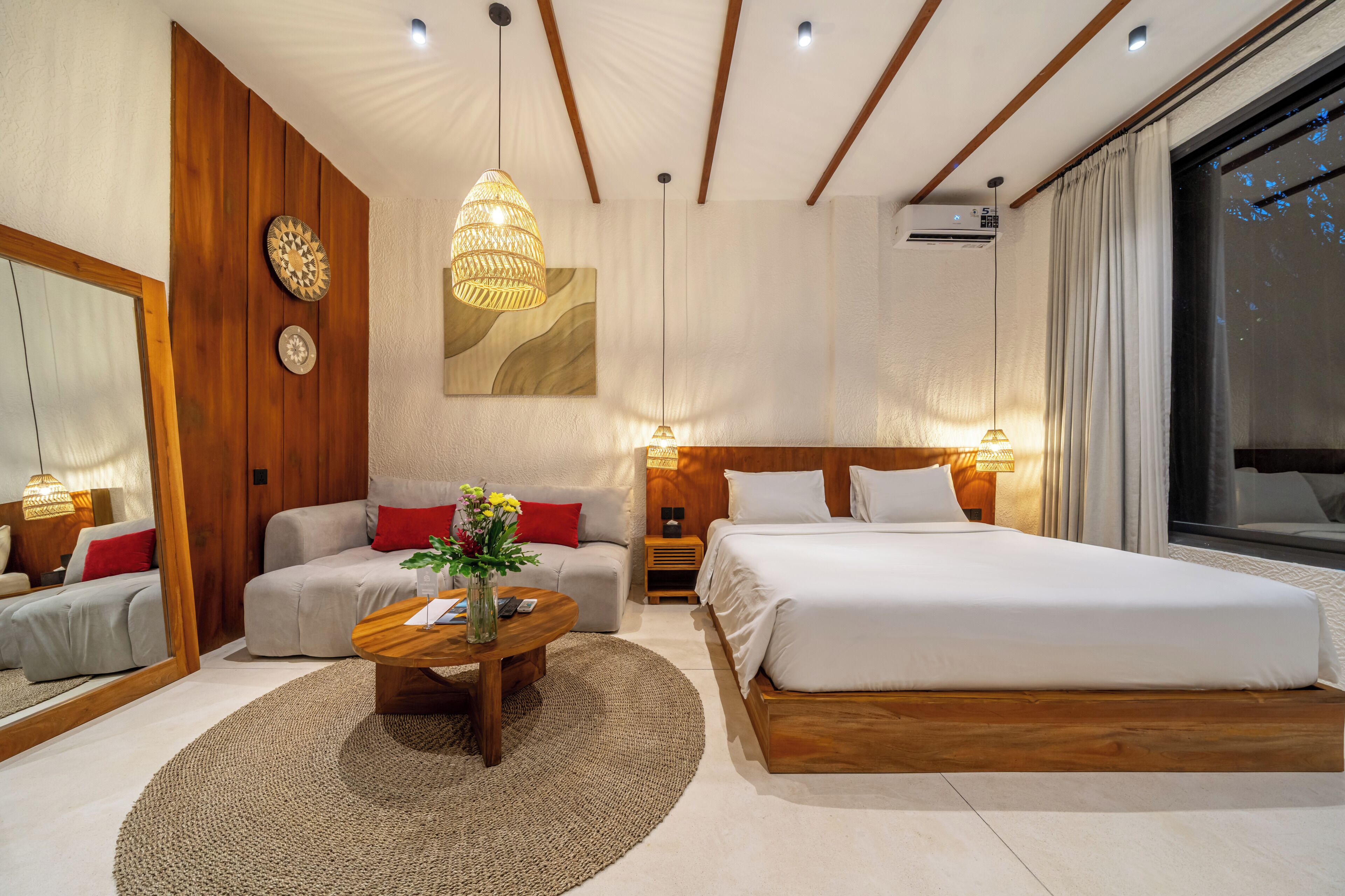 A modern hotel room with a bed, sofa, and a coffee table with a vase of flowers.