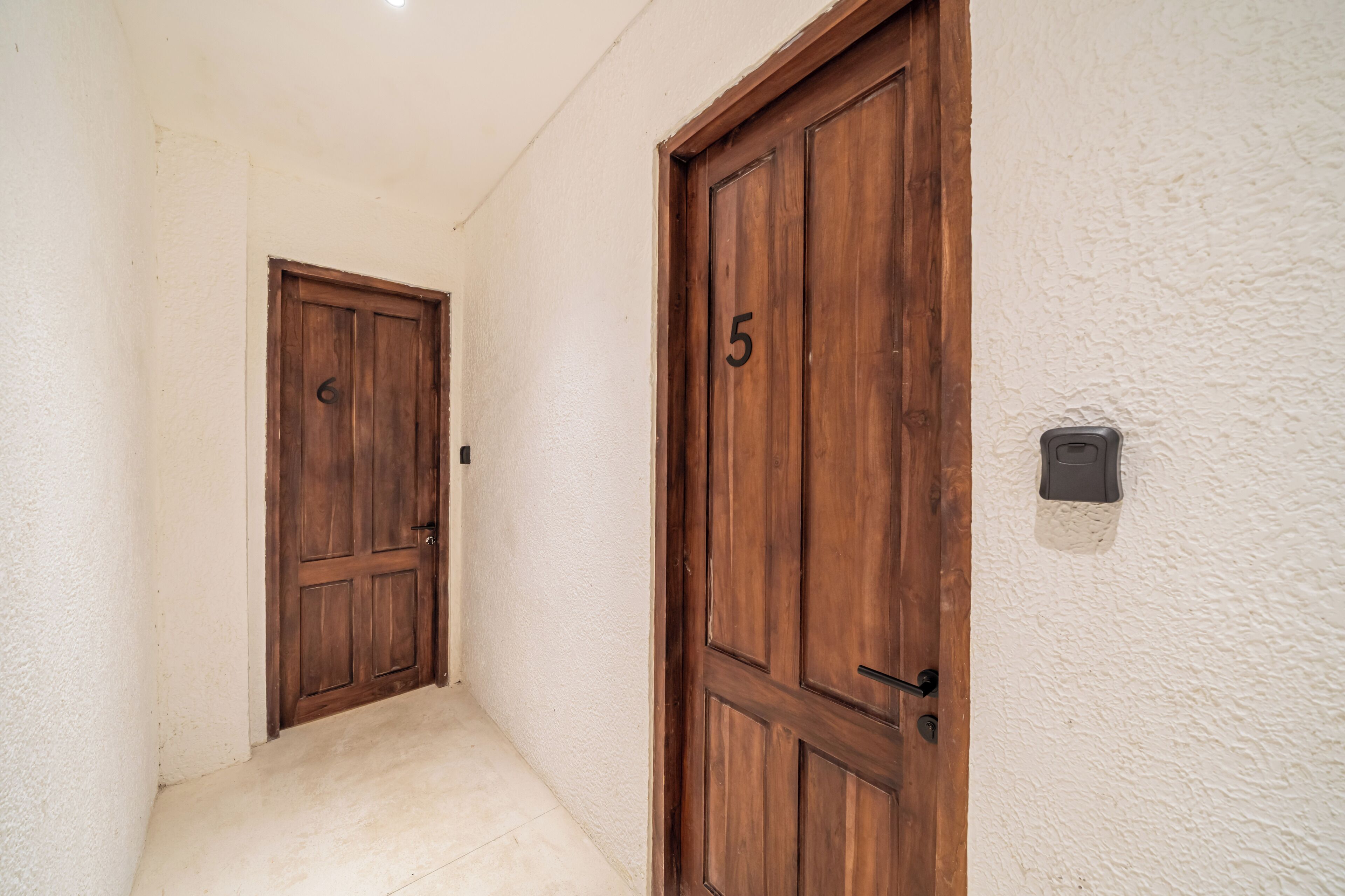 Un pasillo con dos puertas de madera, una con el número 5, y una pared con textura.
